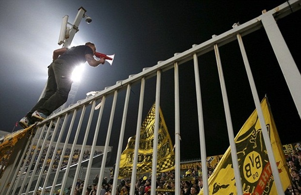 Trưởng nhóm CĐV Borussia Dortmund chông chênh trên tường rào với chiếc loa để bắt nhịp cổ vũ.