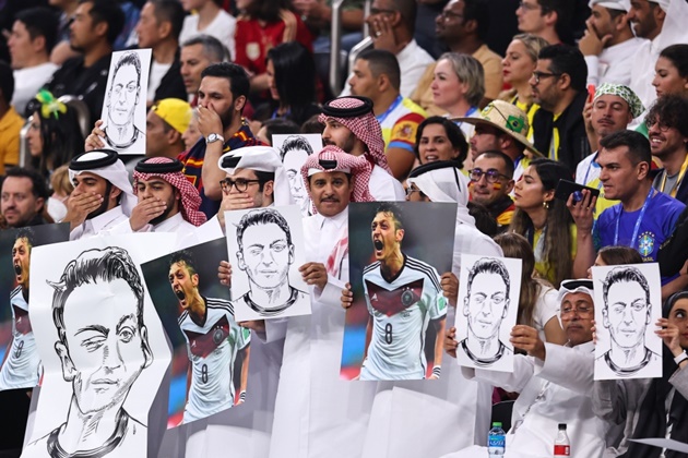 Fans seen holding pictures of Mesut Ozil up while putting hands over mouths during Germany’s World Cup clash against Spain - Bóng Đá