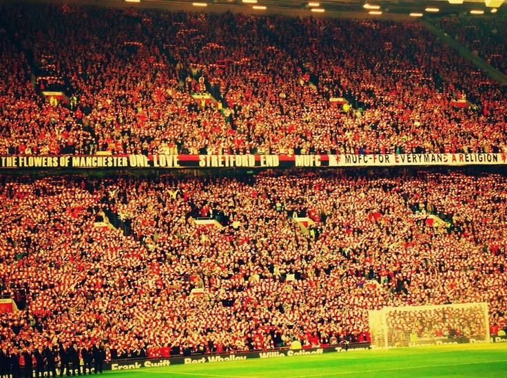 Stretford End chật cứng khán giả, biển người đứng san sát, cùng giơ khăn quàng.