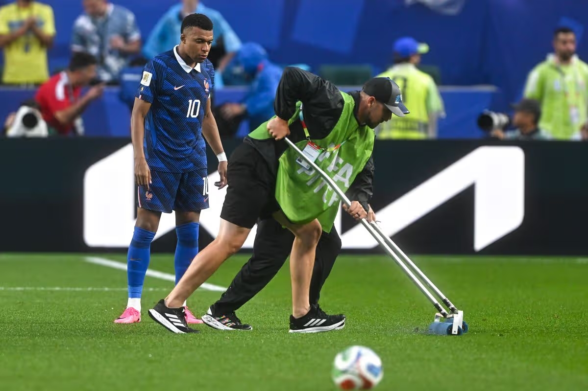 Kylian Mbappe hỗ trợ các nhân viên dọn dẹp mặt cỏ sau cơn bão.